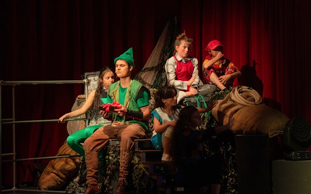 Children in colorful costumes perform a scene from "Zimt & Zauber: THE WIZARD OF OZ" on stage.