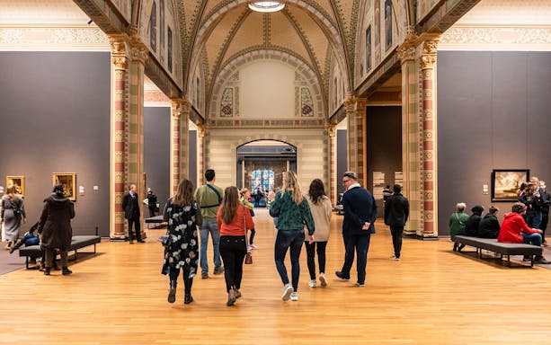 Visitors walking through ornate corridors inside Rijksmuseum, Amsterdam.