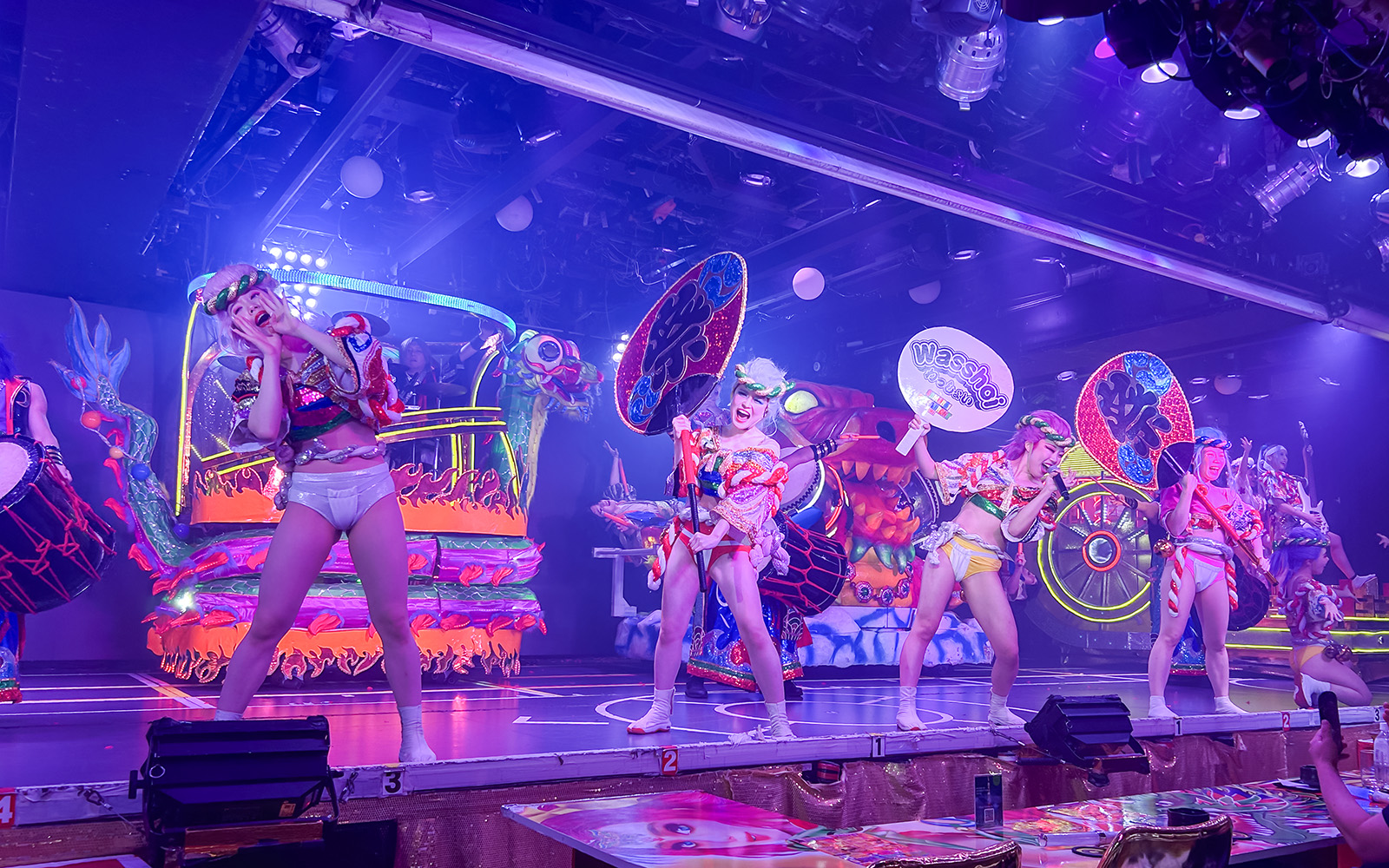 Performers in vibrant costumes on stage at Samurai Restaurant Show, Tokyo, with colorful lights and sound effects.