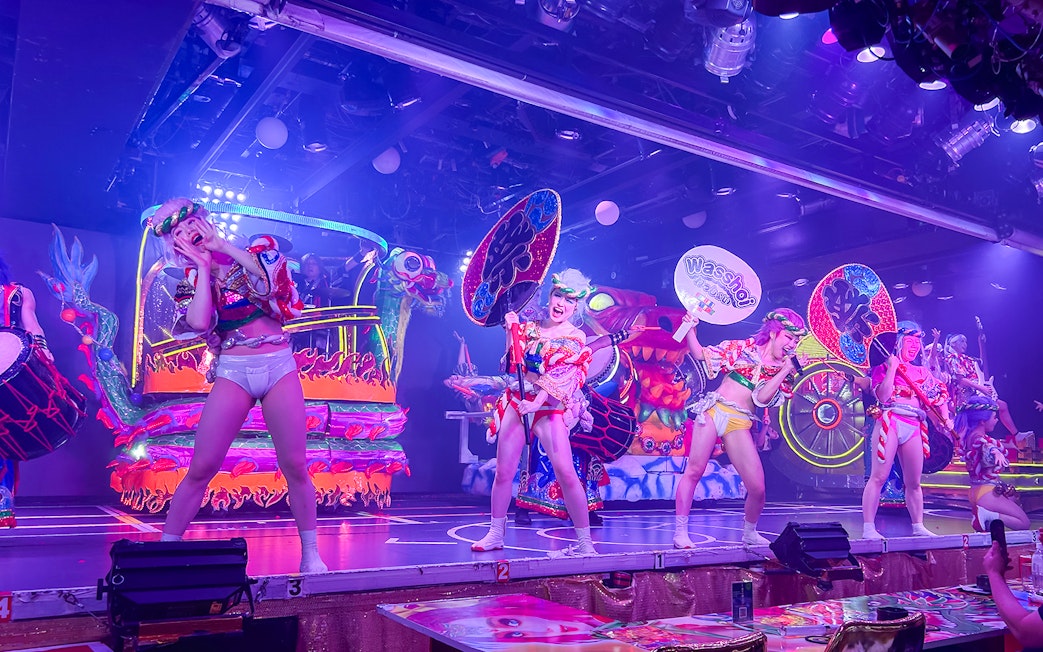 Performers in vibrant costumes on stage at Samurai Restaurant Show, Tokyo, with colorful lights and sound effects.
