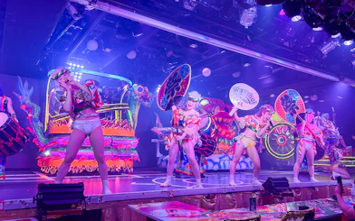 Performers in vibrant costumes on stage at Samurai Restaurant Show, Tokyo, with colorful lights and sound effects.
