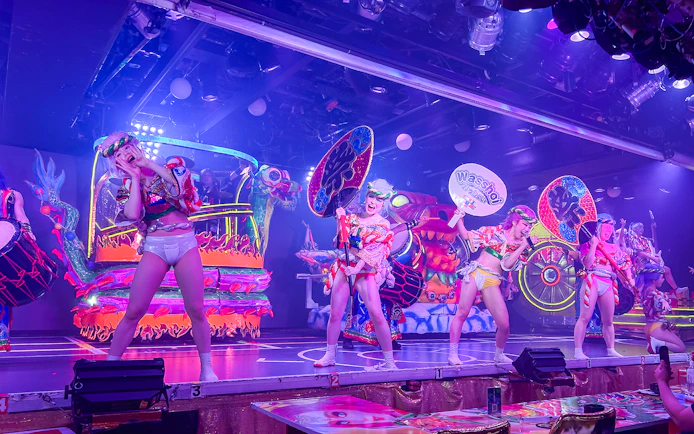 Performers in vibrant costumes on stage at Samurai Restaurant Show, Tokyo, with colorful lights and sound effects.