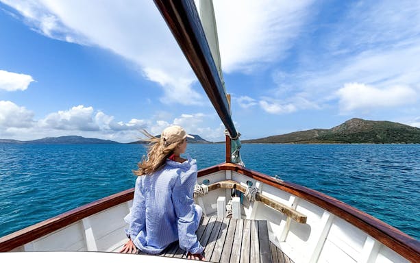Sailing towards Asinara Island on a wooden boat, clear blue sea and distant hills.