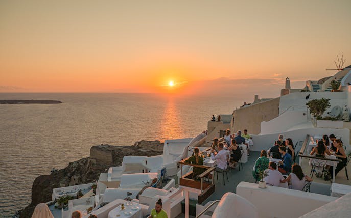 Santorini sunset view with people dining on a terrace overlooking the sea.