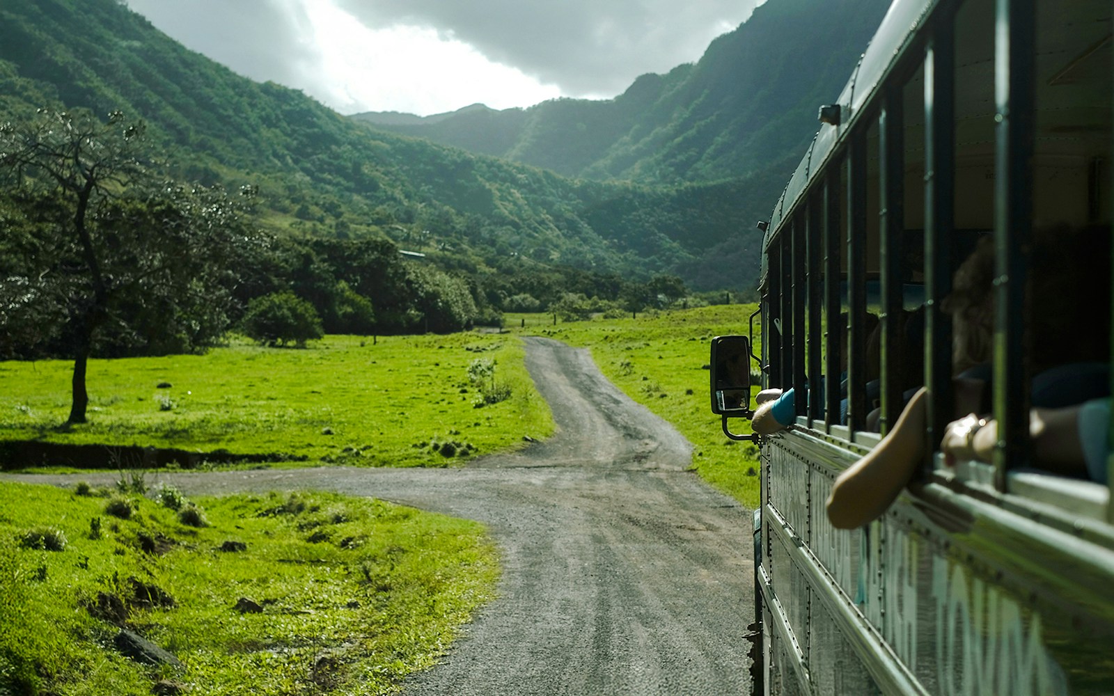 Tour bus on a scenic road through lush green valleys at Kualoa Ranch, Hawaii.