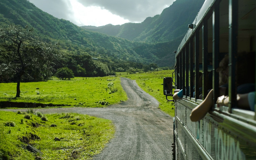 Tour bus on a scenic road through lush green valleys at Kualoa Ranch, Hawaii.