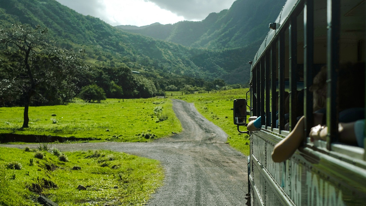 Tour bus on a scenic road through lush green valleys at Kualoa Ranch, Hawaii.