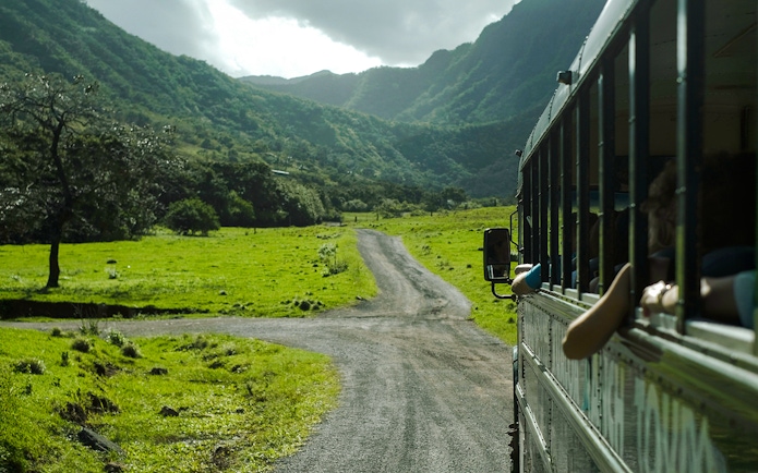 Tour bus on a scenic road through lush green valleys at Kualoa Ranch, Hawaii.
