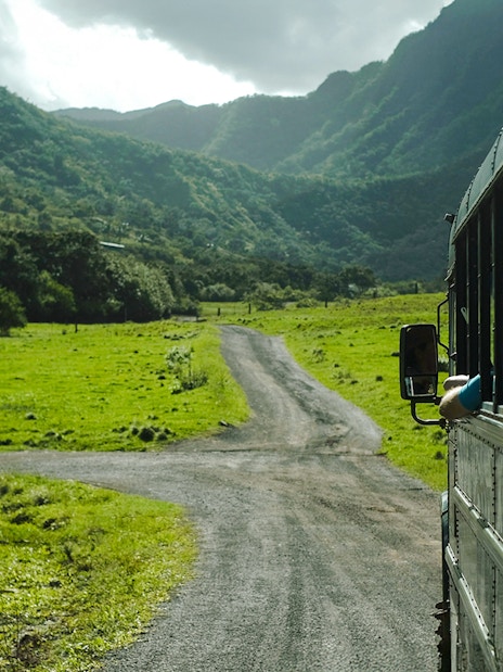 Tour bus on a scenic road through lush green valleys at Kualoa Ranch, Hawaii.
