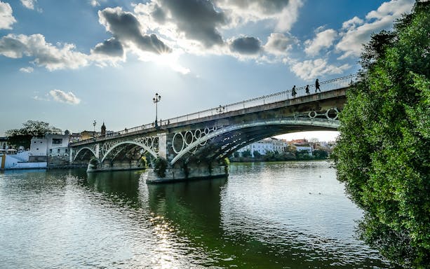 Triana Bridge over the Guadalquivir River in Seville, Spain, with people walking.