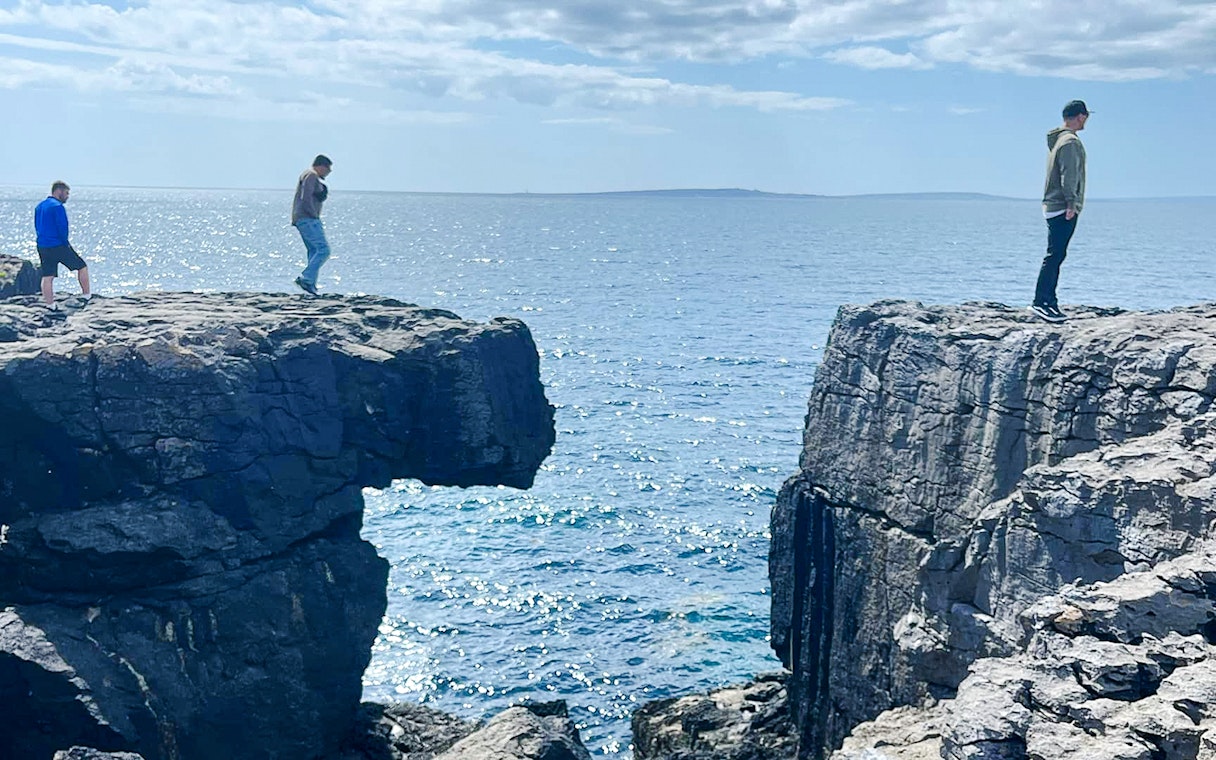 People standing on opposite sides of a gap in the Cliffs of Moher, Ireland, overlooking the ocean.