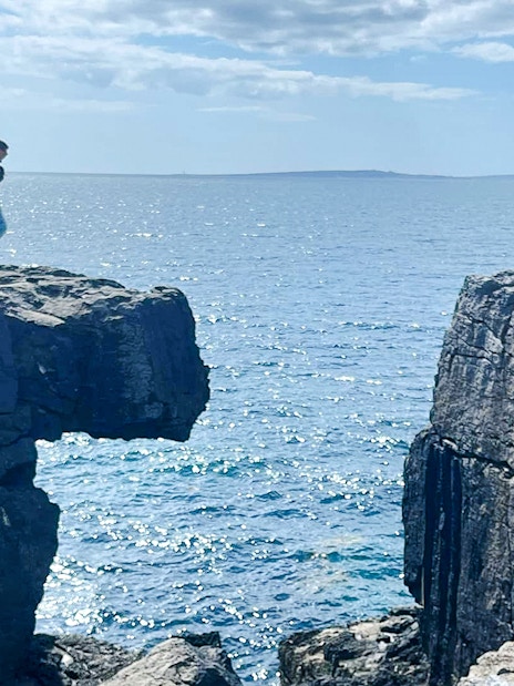 People standing on opposite sides of a gap in the Cliffs of Moher, Ireland, overlooking the ocean.