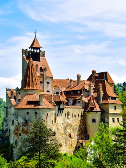 Bran Castle with red-tiled roofs surrounded by greenery in Transylvania.