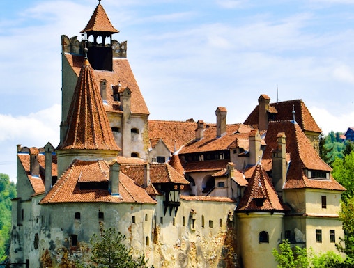Bran Castle with red-tiled roofs surrounded by greenery in Transylvania.