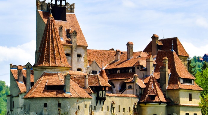 Bran Castle with red-tiled roofs surrounded by greenery in Transylvania.