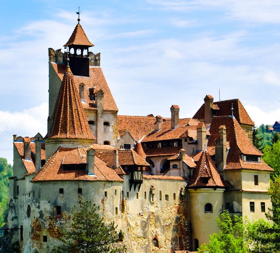 Bran Castle with red-tiled roofs surrounded by greenery in Transylvania.