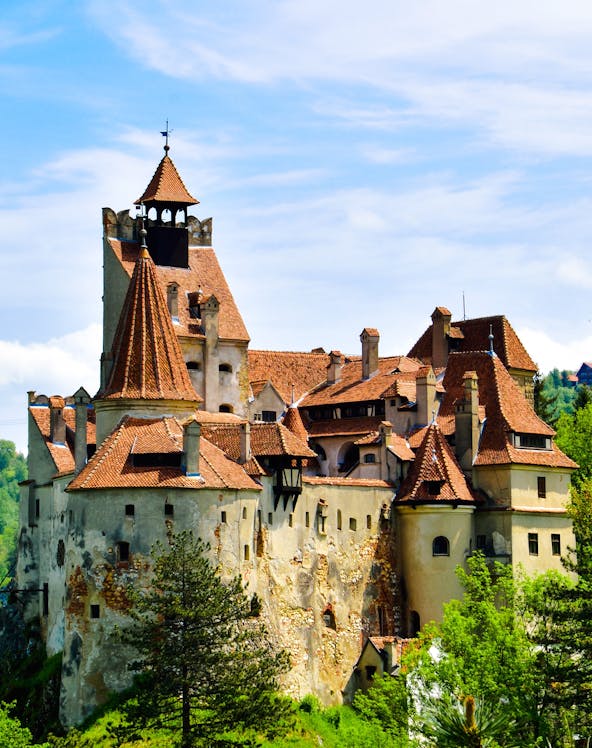 Bran Castle with red-tiled roofs surrounded by greenery in Transylvania.