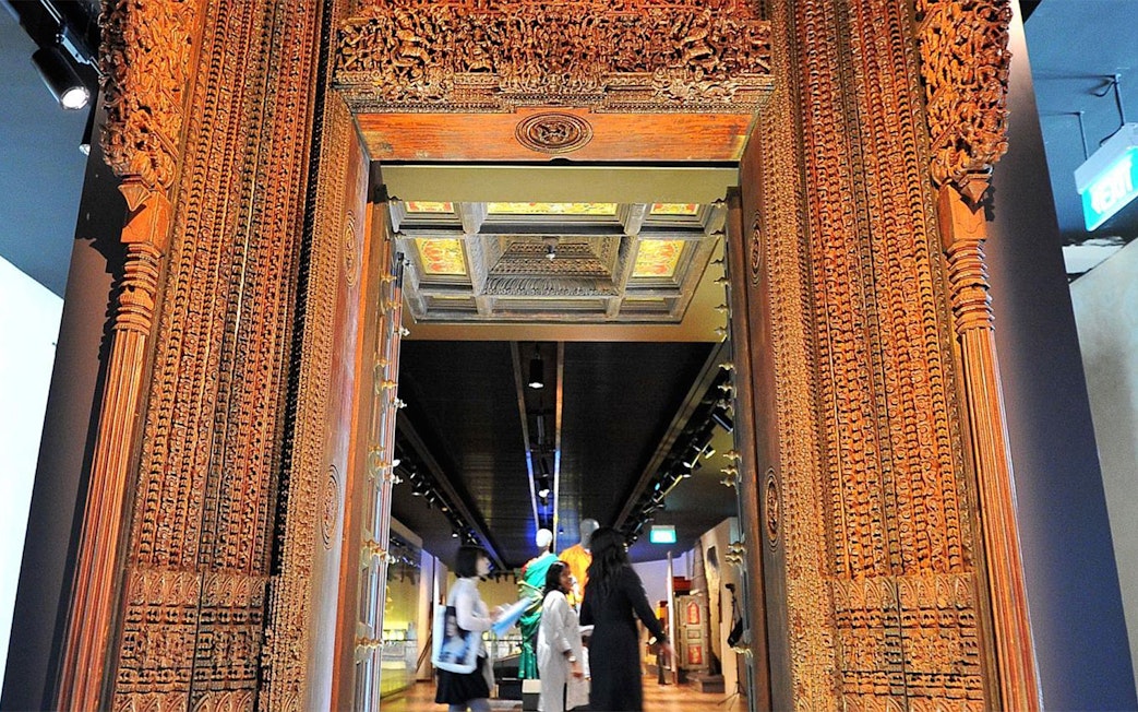 Visitors explore the Indian Heritage Centre through a carved wooden doorway.