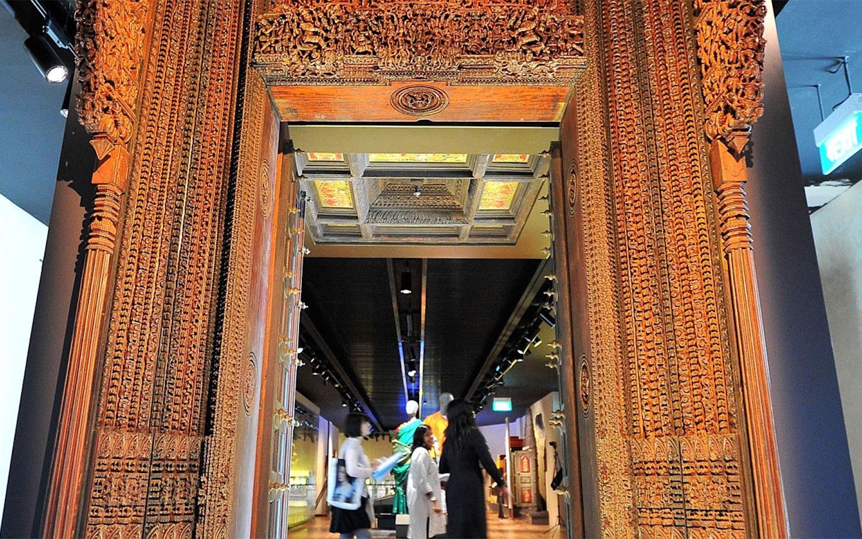 Visitors explore the Indian Heritage Centre through a carved wooden doorway.