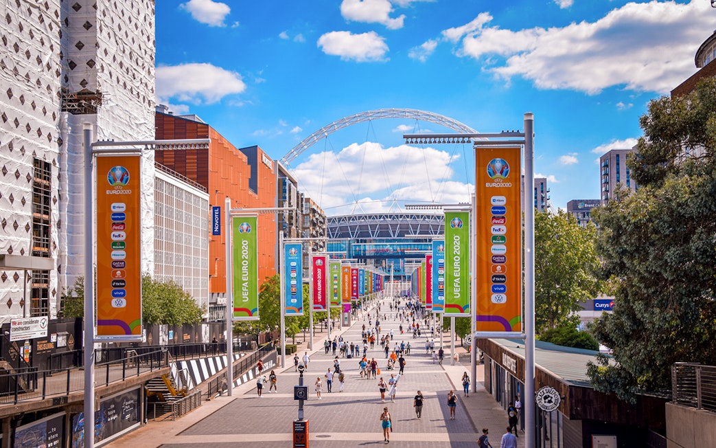 Wembley Stadium entrance with colorful UEFA Euro 2020 banners and visitors walking.