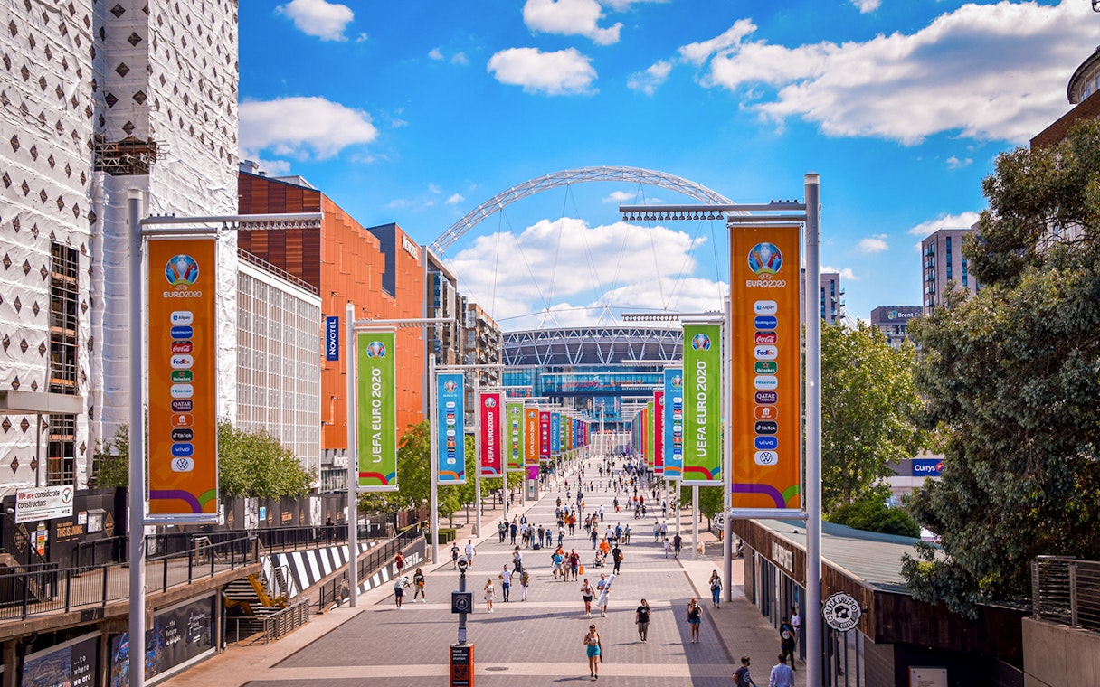 Wembley Stadium entrance with colorful UEFA Euro 2020 banners and visitors walking.