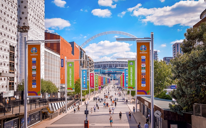 Wembley Stadium entrance with colorful UEFA Euro 2020 banners and visitors walking.