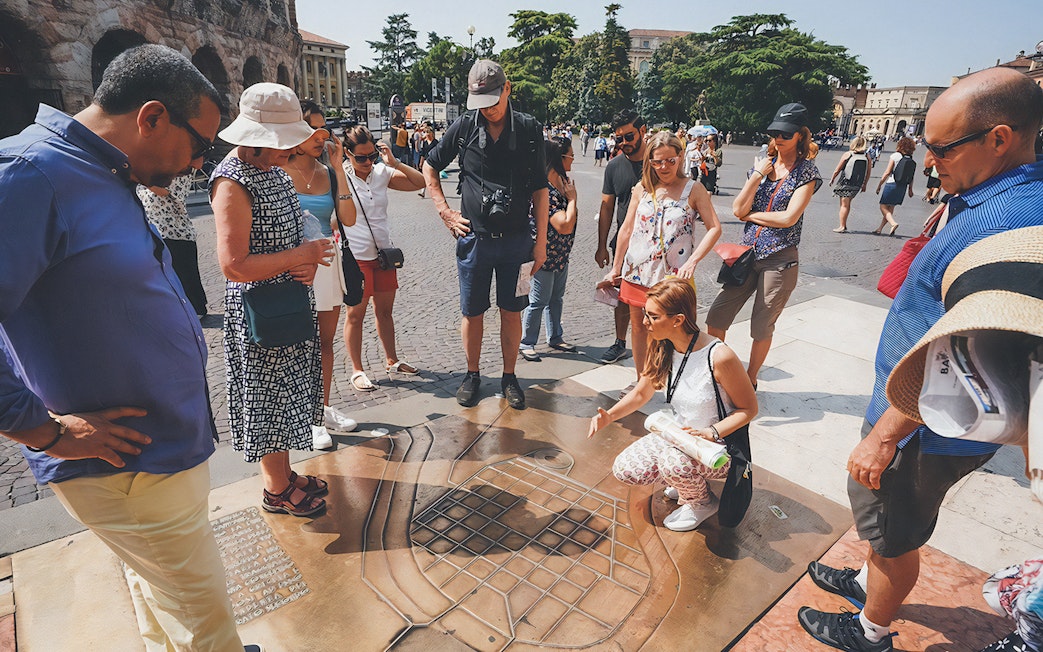 Tour guide explaining Verona Arena map to tourists outside the amphitheater.