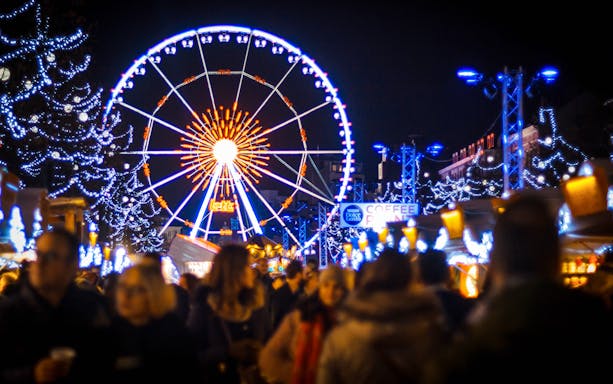 Ferris wheel and festive lights at a bustling Christmas market.