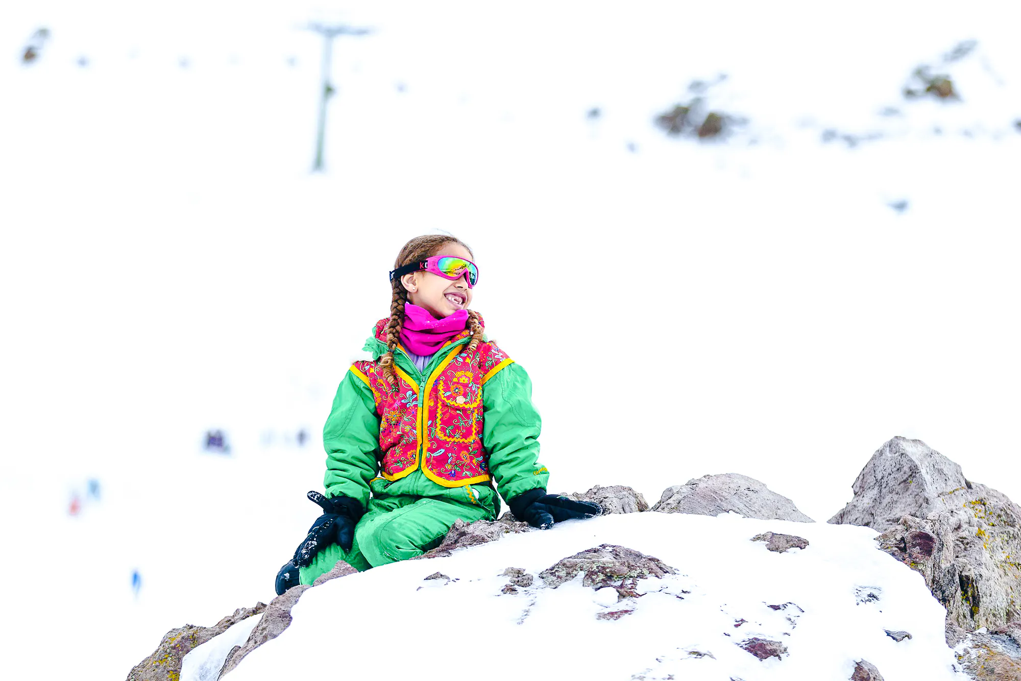 Child in colorful snow gear sitting on rocks at Farellones Park, Santiago.