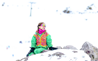 Child in colorful snow gear sitting on rocks at Farellones Park, Santiago.