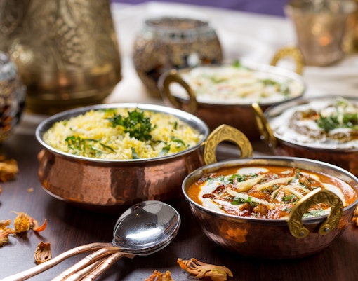 Copper bowls with Indian curry, rice, and yogurt dishes on a wooden table.