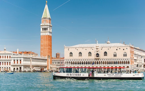 Venice canal with St. Mark's Campanile and Doge's Palace, featuring a city cruise boat.