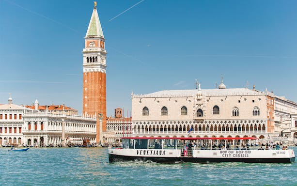Venice canal with St. Mark's Campanile and Doge's Palace, featuring a city cruise boat.