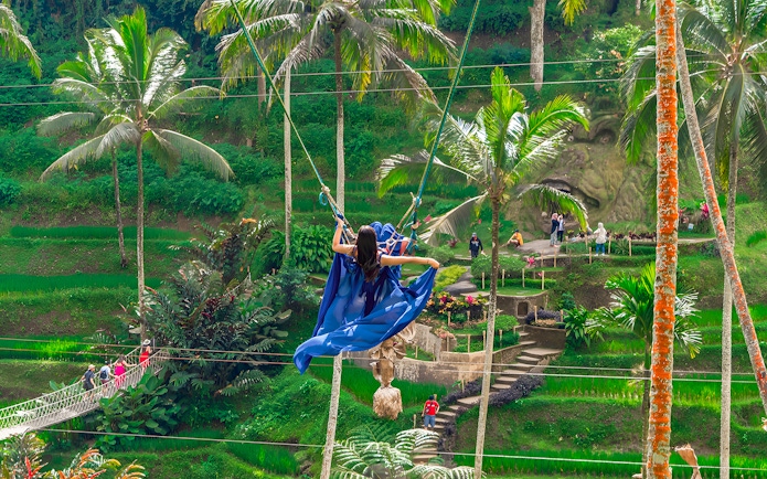 Woman on swing at Alas Harum Bali with lush greenery and palm trees.