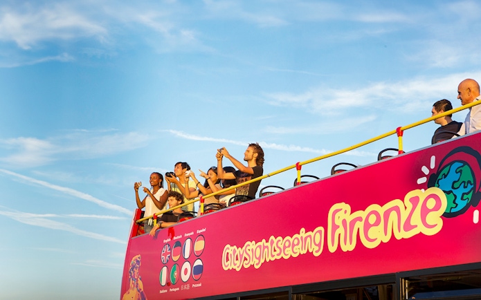 Tourists on an open-top sightseeing bus in Florence, Italy, taking photos.