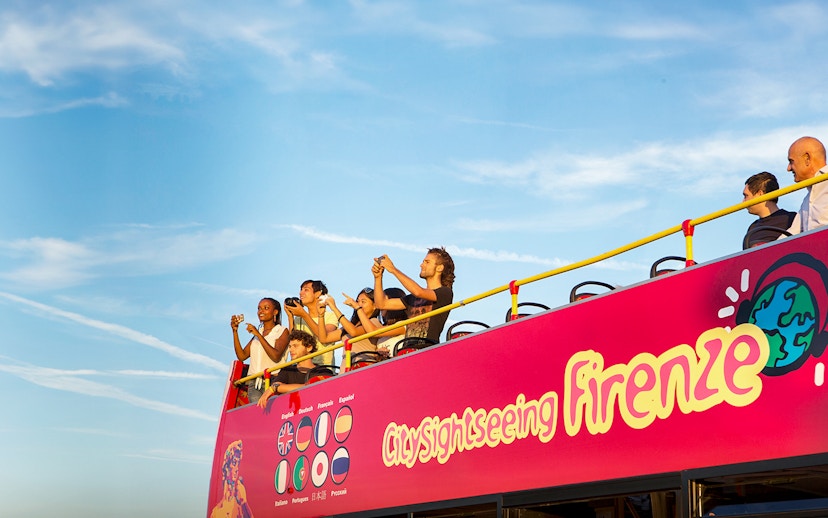Tourists on an open-top sightseeing bus in Florence, Italy, taking photos.