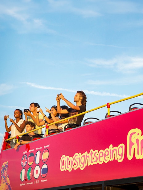 Tourists on an open-top sightseeing bus in Florence, Italy, taking photos.