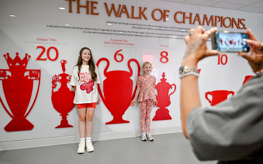 Children posing by the trophy wall at Liverpool FC's Anfield stadium.