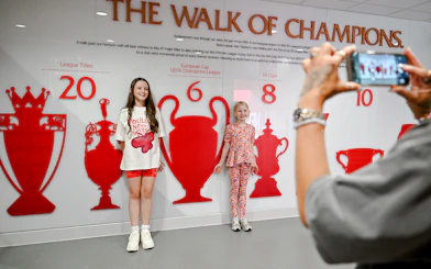Children posing by the trophy wall at Liverpool FC's Anfield stadium.