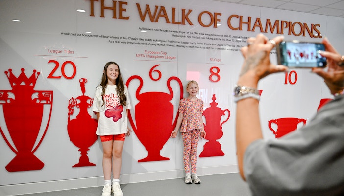Children posing by the trophy wall at Liverpool FC's Anfield stadium.