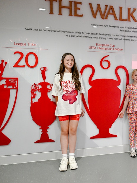 Children posing by the trophy wall at Liverpool FC's Anfield stadium.