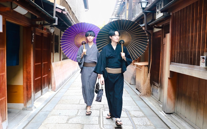 Individuals in traditional yukata walking with umbrellas on a Kyoto street.
