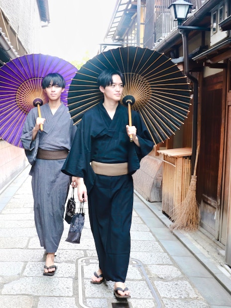 Individuals in traditional yukata walking with umbrellas on a Kyoto street.