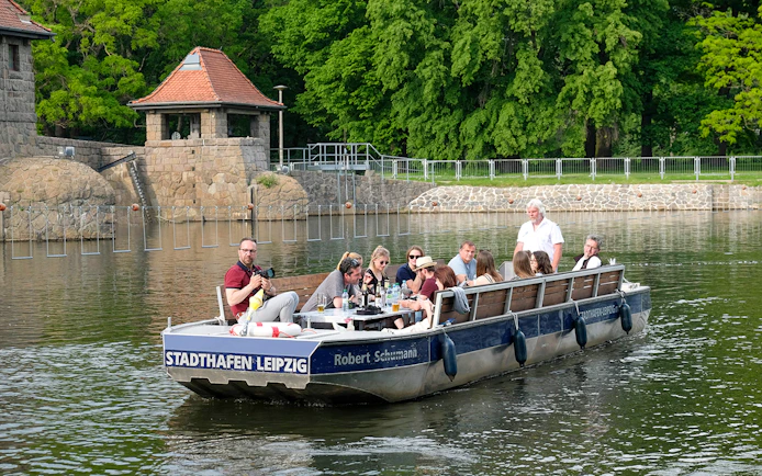 Guests on a motorboat tour of Karl Heine Canal in Leipzig, passing stone buildings and greenery.