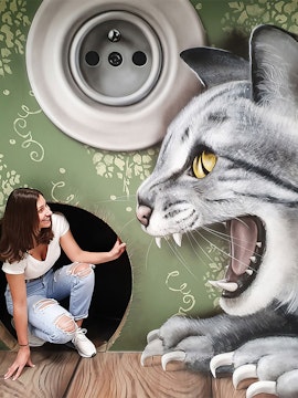 Woman interacting with giant cat illusion at Museum of Fantastic Illusions.
