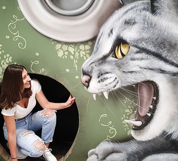 Woman interacting with giant cat illusion at Museum of Fantastic Illusions.