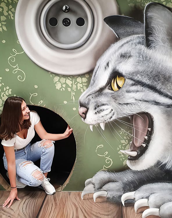 Woman interacting with giant cat illusion at Museum of Fantastic Illusions.