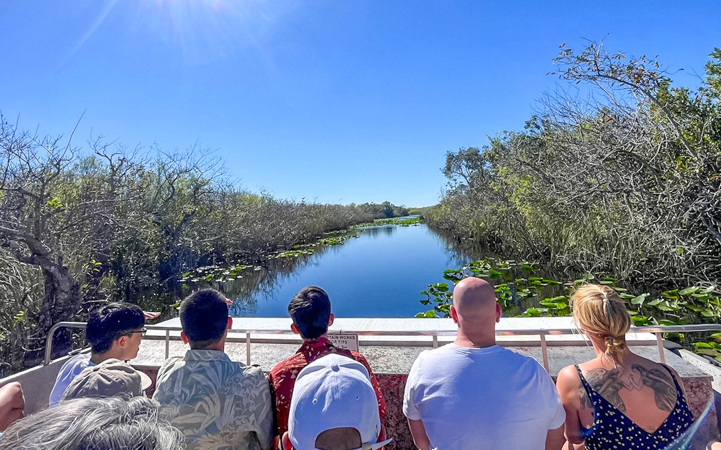 Tourists on an airboat in Everglades National Park, Miami, surrounded by water and vegetation.