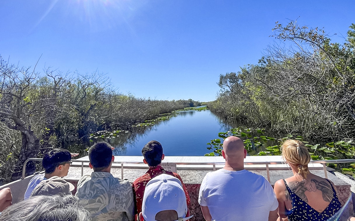 Tourists on an airboat in Everglades National Park, Miami, surrounded by water and vegetation.
