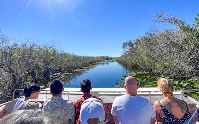 Tourists on an airboat in Everglades National Park, Miami, surrounded by water and vegetation.